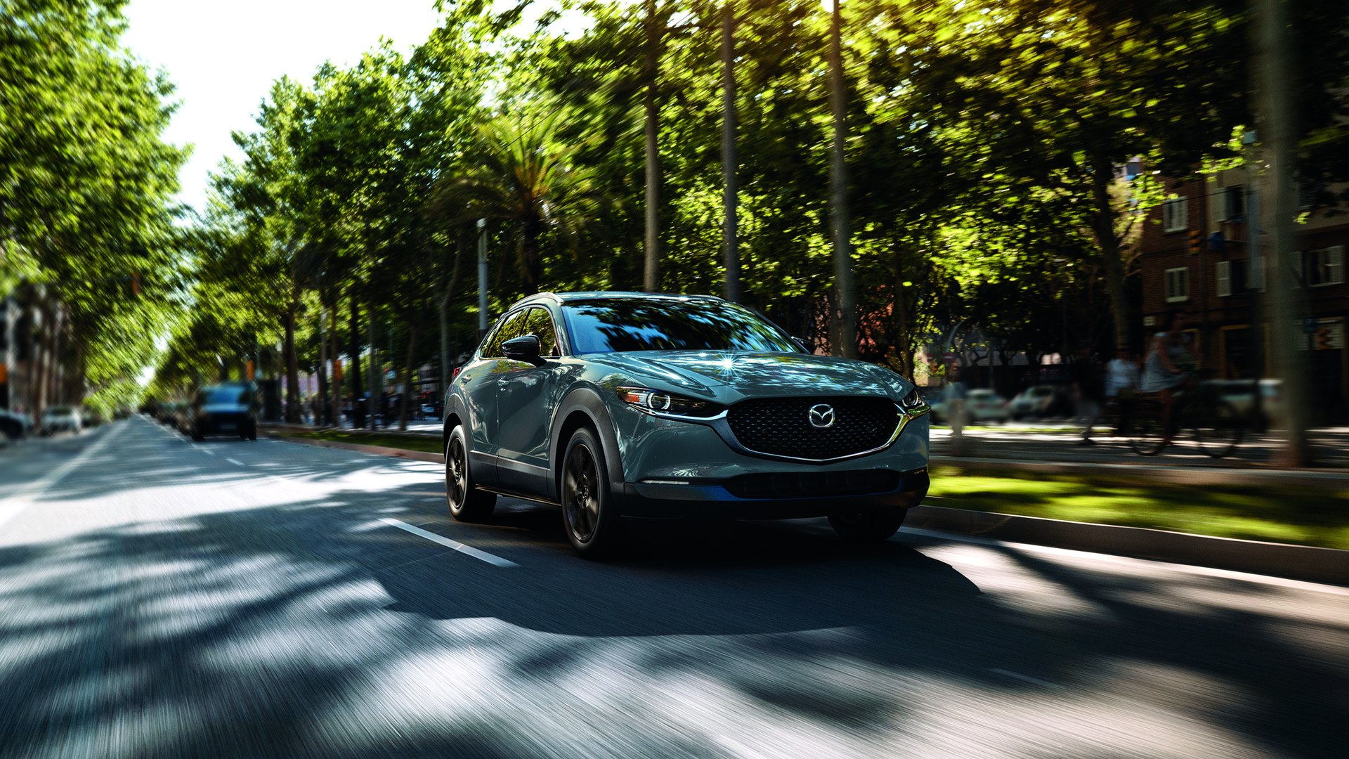 Mazda CX-30 2022 gris, vue trois-quarts avant en conduite dans une rue bordée d'arbres