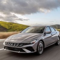 Elantra 2024 restylée argent, vue trois-quarts avant en conduite sur route de collines | Hyundai Elantra 2024 restylée argent, vue trois-quarts avant en conduite sur route de collines