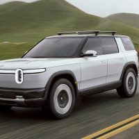Rivian R2 de présentation 2024, gris pâle, en vue trois-quarts avant sur une route vallonnée | Rivian Rivian R2 de présentation 2024, gris pâle, roulant sur une route de campagne bordée de collines, vu de trois-quarts avant