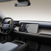 Habitacle du Rivian R2 de présentation 2024, avec la planche de bord, le volant et l'écran central | Rivian Habitacle complet du Rivian R2 de présentation 2024 aux tons bleu ardoise, avec la planche de bord, le volant, l'écran central et la console vus du côté passager