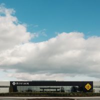 Entrée de l'usine Rivian de Normal, en Illinois, photographiée en 2021 | Rivian Façade de l'usine Rivian de Normal, en Illinois, avec le logo Rivian, sous un ciel nuageux, en 2021