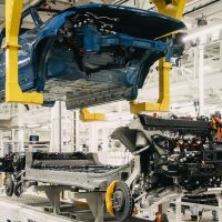 Usine de Normal en 2021 : la caisse d'un Rivian R1 descend vers sa plateforme à batterie sur la chaîne d'assemblage | Rivian Caisse bleue d'un Rivian R1 suspendue au-dessus de sa plateforme avec batterie, roues et moteurs, sur la chaîne d'assemblage de l'usine Rivian de Normal en 2021