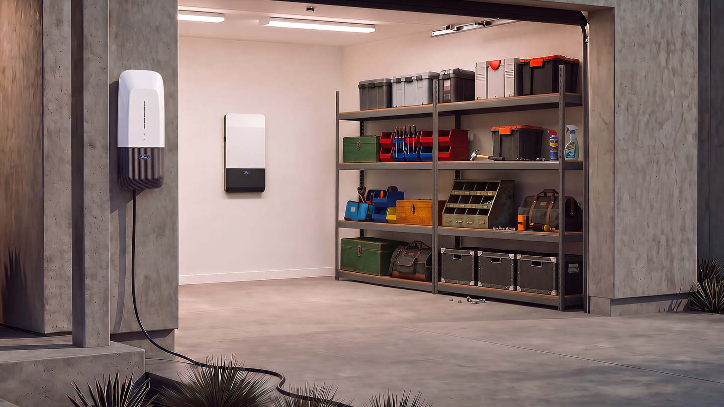 Prototype de la Ford Home Power Station avec câble de recharge sur un pilier de garage, et Ford Home Backup Power Panel fixé au mur du garage, à côté d'étagères de rangement
