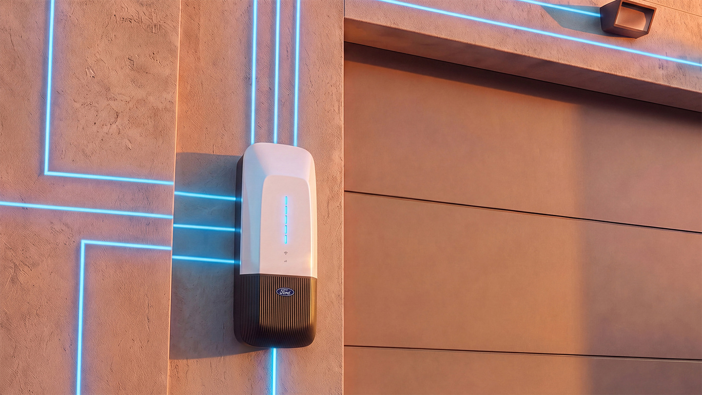 Prototype de la Ford Home Power Station pour l'alimentation bidirectionnelle du Ford Fathom, fixé à un mur extérieur près d'une porte de garage, avec des lignes bleues lumineuses illustrant la circulation de l'énergie