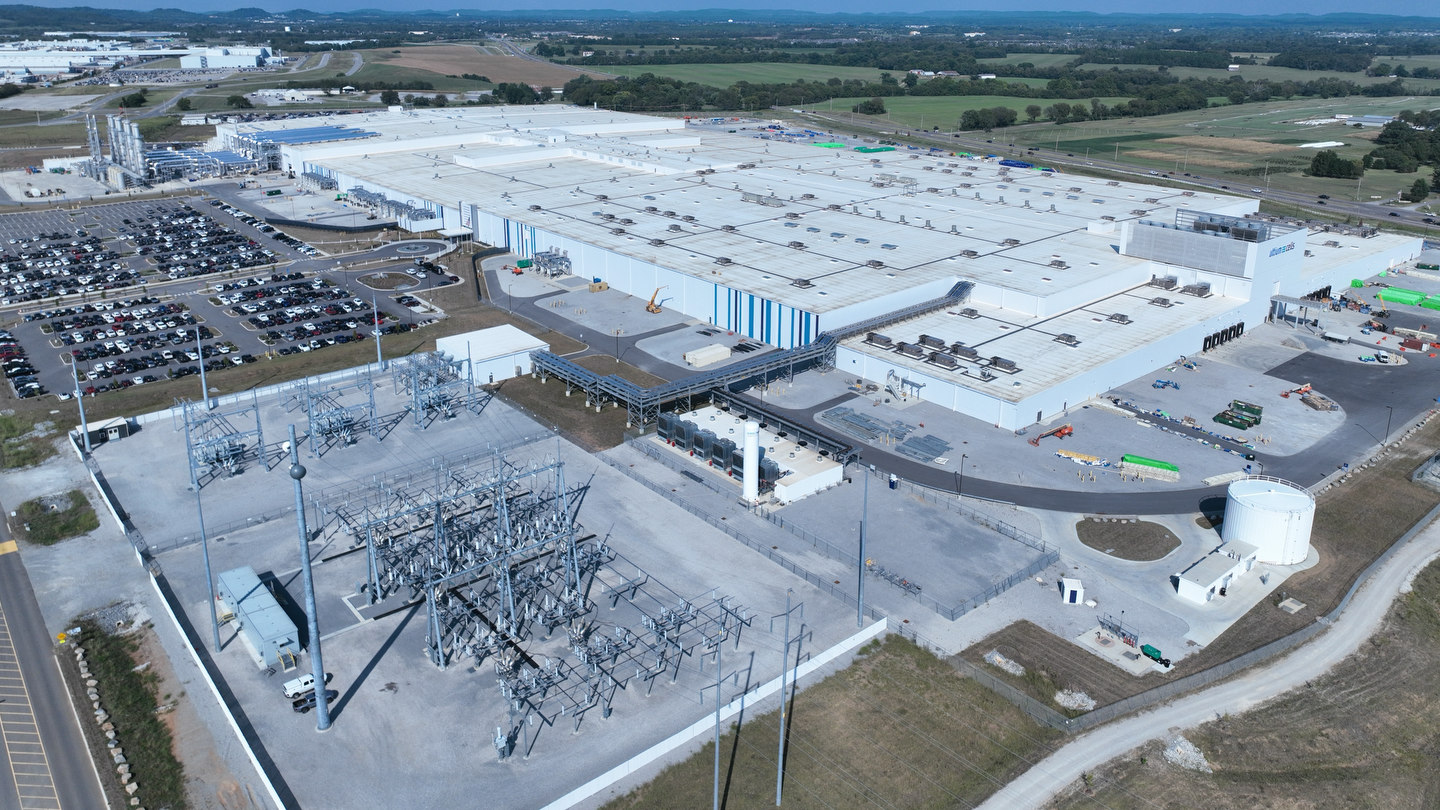 Vue aérienne élargie de l'usine de batteries d'Ultium Cells à Spring Hill, au Tennessee, avec un poste électrique, le stationnement des employés et des terres agricoles.